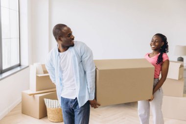 Young African American couple joyfully carrying a large cardboard box while moving into their bright new apartment, embracing fresh beginnings