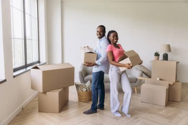 Young African American couple moving into a new apartment, carrying cardboard boxes and smiling joyfully at their fresh start