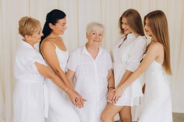 Four women of different generations, dressed in elegant white, holding hands, celebrating family bonds and togetherness