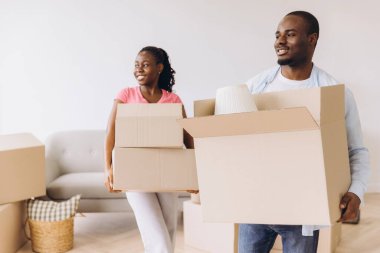 Smiling african american couple carrying cardboard boxes moving into new home, starting new life together