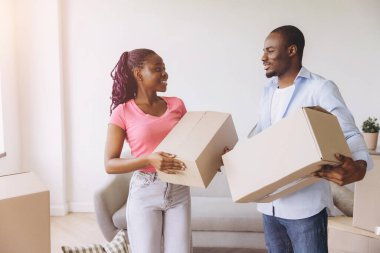 Smiling african american couple carrying cardboard boxes, relocating to new apartment, purchasing real estate, starting new life together