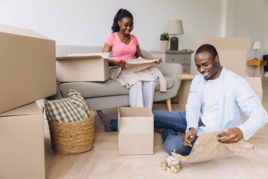Young black couple unpacking clothes and personal belongings from cardboard boxes in new apartment