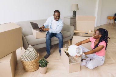 Happy african american couple unpacking belongings from cardboard boxes in new apartment, starting new life chapter together