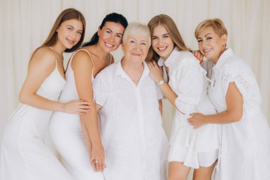 Five women of different generations wearing white dresses are posing together, creating a portrait that celebrates family ties and togetherness