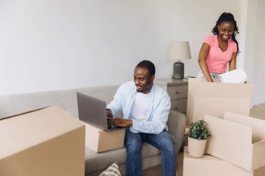 Happy African American couple moving into a new apartment, unpacking boxes and using a laptop to settle into their fresh space