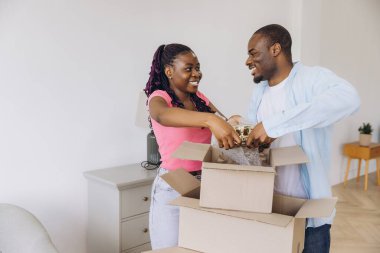Young couple smiling while unpacking household items from cardboard boxes in their new apartment, embracing the excitement of fresh beginnings