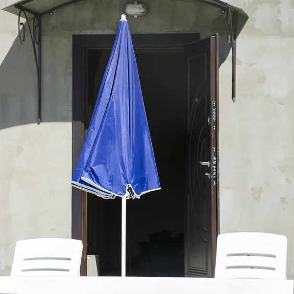İki beyaz güneşlenme sandalyeli yanındaki mavi şemsiye