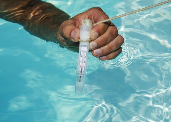 Primer plano del termómetro de la piscina en la mano del hombre, el agua de la piscina es caliente . —  Fotos de Stock