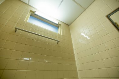 Kare duvarda asılı alüminyum havlu askısı ve banyoda penceresi var.