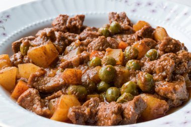 Türk geleneksel tas kebabı patates, bezelye ve domates beyaz bir tabak içinde. Organik sulu et güveç.