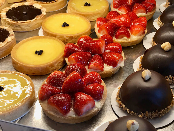 Pastry shop with variety of tarts, cakes, creme brulee, with strawberry, chocolate, lemon, pears and apple slices displayed at showcase. Organic Food.