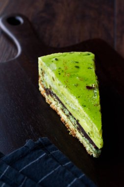 Matcha yeşil çay katman pasta dilimi koyu ahşap tahta üzerinde. Organik tatlı.