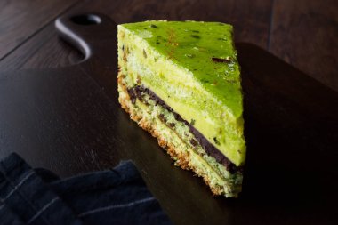 Matcha yeşil çay katman pasta dilimi koyu ahşap tahta üzerinde. Organik tatlı.