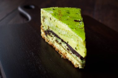 Matcha yeşil çay katman pasta dilimi koyu ahşap tahta üzerinde. Organik tatlı.