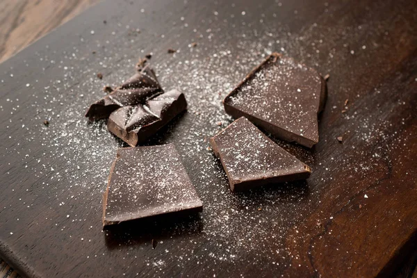 Koyu ahşap yüzey üzerinde deniz tuzu ile acı çikolata parçaları. Organik aperatifler.