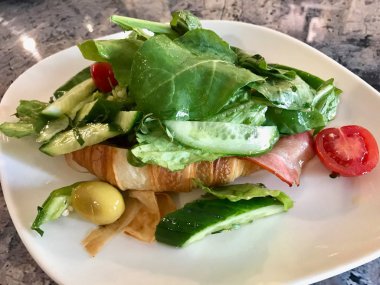 Pastırmalı Kruvasan Sandviç ve Çedar Peynirli Salata, Yeşil Zeytin, Salatalık ve Çeri Domates ile servis edilir