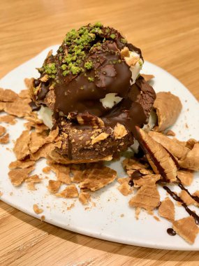 Dondurma Tabakta Koni Parçaları, Çikolata Sosu ve Antep Fıstığı Tozu ile servis.