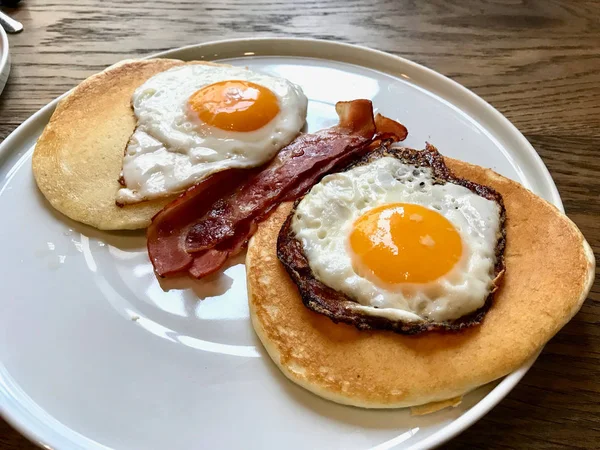 Aussie / australisches Frühstück mit Brioche-Toast, Spiegeleiern, knuspriger Speckwurst, salzigen Pfannkuchen und Pilzen. — Stockfoto