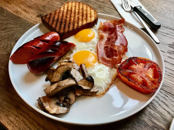 Aussie / australisches Frühstück mit Brioche-Toast, Spiegeleiern, knuspriger Speckwurst, salzigen Pfannkuchen und Pilzen. — Stockfoto