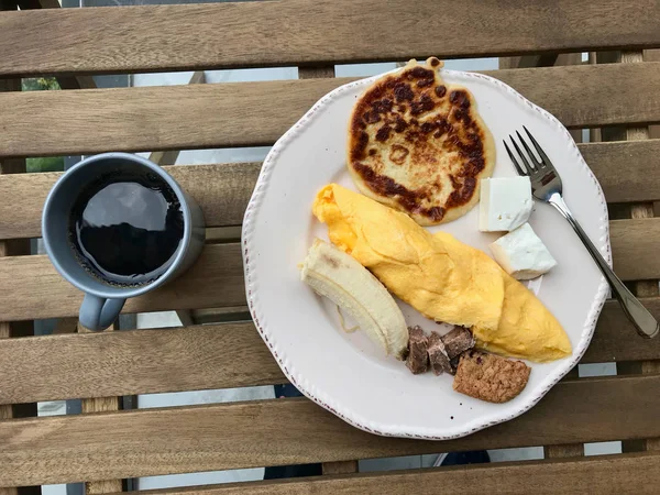 Desayuno de tortitas con tortilla francesa, plátano, carne, galletas, queso y café en la mesa de madera . — Foto de Stock