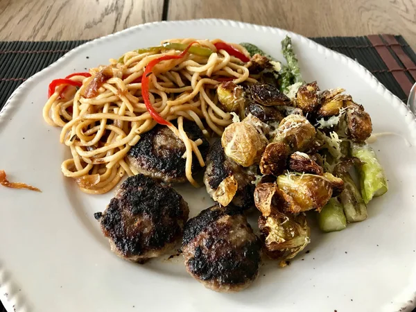 Piatto di polpette fatte in casa con tagliatelle, cavoletti di Bruxelles arrosto e asparagi . — Foto Stock