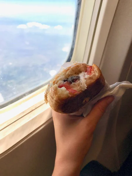 Sandwich in Plane Cabin Economy Class Holding with Hand next to Window View.