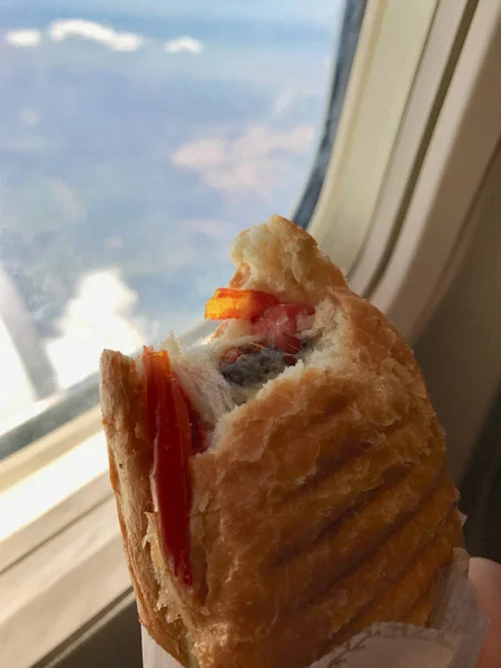 Sandwich in Plane Cabin Economy Class Holding with Hand next to Window View.