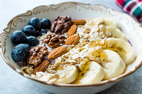 Acai Bowl with Yogurt, Blackberry, Banana Slices, Walnut, Honey, Jam, Oat, Almond, Sesame Seeds and Granola in Porcelain Bowl.