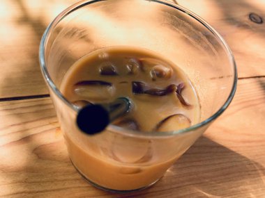 Siyah Saman ile Ahşap Masa üzerinde Süt ve Buz Küpleri ile Buzlu Americano. 