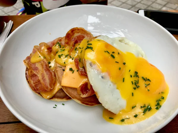 Zoute pannenkoeken met hollandaise saus, gesmolten cheddar kaas, eieren en knapperige bacon voor het ontbijt. — Stockfoto