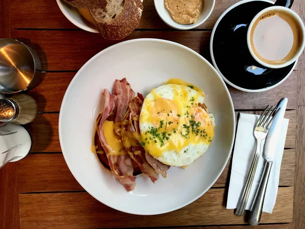 Salta pannkakor med hollandaisesås, smält cheddarost, ägg och krispig bacon till frukost med kaffe. — Stockfoto
