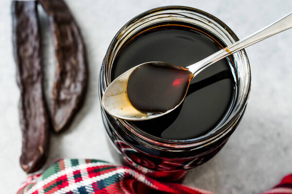 Carob Molasses Dripping from Spoon to Jar.