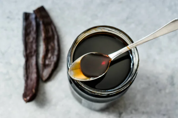 Johannesbrood melasse druipend van lepel naar pot. — Stockfoto