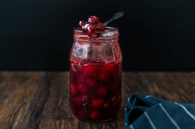 Kavanozda kızılcık reçeli ve kaşık / kızılcık reçeli ile kahvaltı için ekmek dilimleri servis ediliyor..