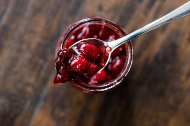 Kavanozda kızılcık reçeli ve kaşık / kızılcık reçeli ile kahvaltı için ekmek dilimleri servis ediliyor..