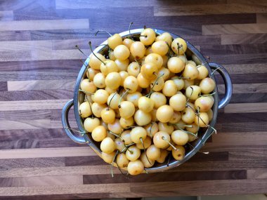 Mutfak tahtadan yüzeyinde Metal Kolander içinde taze sarı kirazlar. Yemeye hazır..