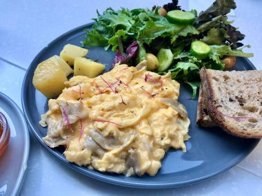 Cafe Restoran 'da çırpılmış yumurta, mantar, kruvasan, ekşi ekmek ve salata ile kahvaltı tabağı.