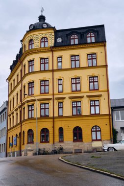 Karlskrona, İsveç; 14 Eylül 2025: Karlskrona 'da Iconic sarı ve omber köşeli bina, Fildişi Pontiac Bonneville klasik Amerikan arabası ıslak sokağa park edilmiş.