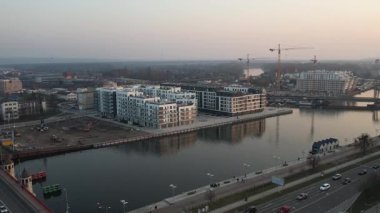 Polonya 'nın Szczecin kentinin hava perspektifi, Odra Nehri boyunca çağdaş kentsel gelişimi sergiliyor. Ön planda, geniş bir yol ve nehir kenarındaki gezinti alanı suya paraleldir. Manzara, yeni ve çağdaş bir konut kompleksini vurguluyor.