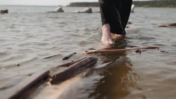Piernas en pantalones negros de un hombre caminar sobre un tronco flotando en el agua — Vídeos de Stock