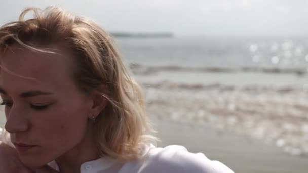 Блондинка чуттєво танцює на фоні моря в білому одязі — стокове відео