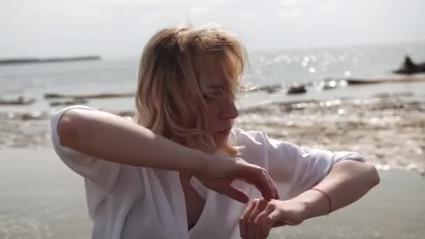 Блондинка чуттєво танцює на фоні моря в білому одязі — стокове відео