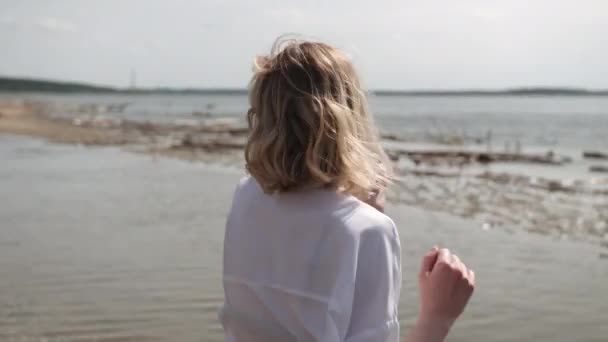 Блондинка чувственно танцует на фоне моря в белой одежде — стоковое видео