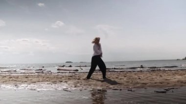 Sarışın kız denizin arka planında beyaz ve siyah kıyafetlerle dans ediyor.