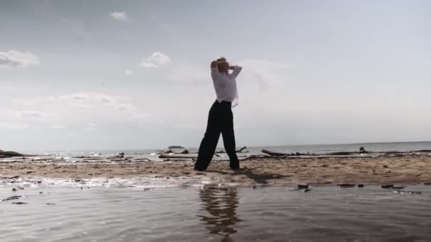 Ξανθιά κοπέλα που χορεύει αισθησιακά σε φόντο θάλασσας με άσπρα και μαύρα ρούχα — Αρχείο Βίντεο