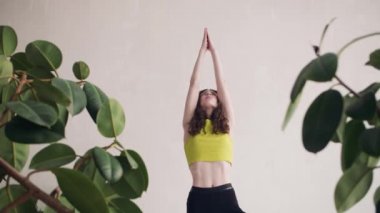Kız, Asana 'nın pozisyonlarından birinde duruyor. Yoga egzersizleri sarı bluzlu güzel bir genç kız yapar.