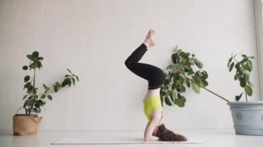 Yoga hocası egzersiz yapar. Ellerinin ve kafasının üstünde duruyor, bacaklarını kaldırıyor.