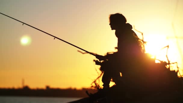 Силует рибалки, який сидить на дереві і ловить рибу на фоні заходу сонця — стокове відео