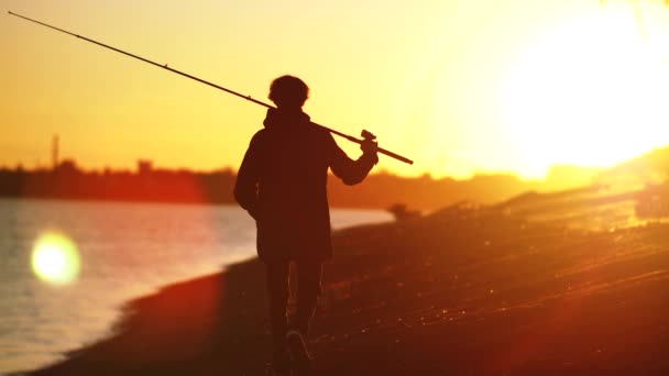 En fiskare går längs stadens strand mot bakgrund av en vacker stads solnedgång — Stockvideo