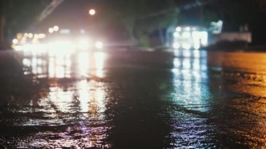 Şehir yolunda dikkati dağıt. Yağmurdan sonra yolun durağan bir çerçevesi. Arabalar geçer ve farlar su birikintilerini yansıtır.
